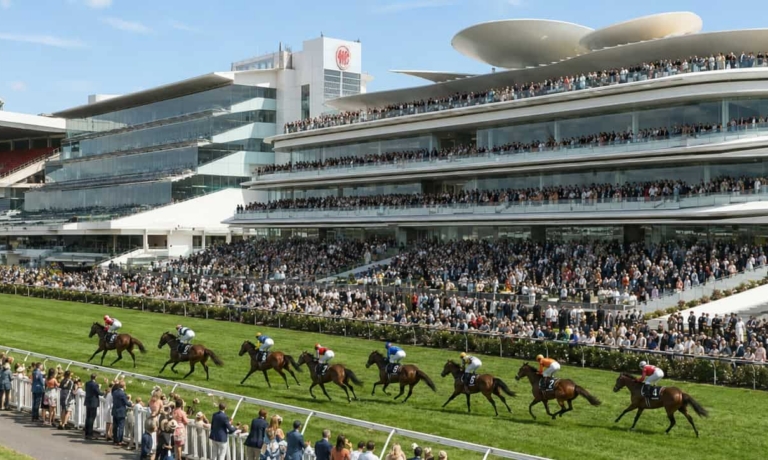 Grandstand filled with spectators at a horse race as horses run on a sunny track, with a modern multi-tiered venue in the background.