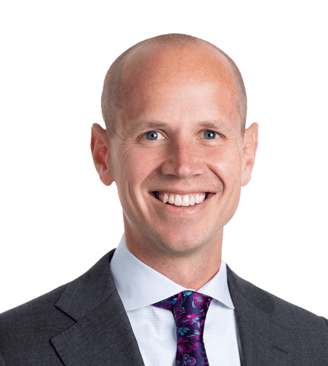 Smiling head-and-shoulders portrait of a bald man in a dark suit and purple tie facing the camera.